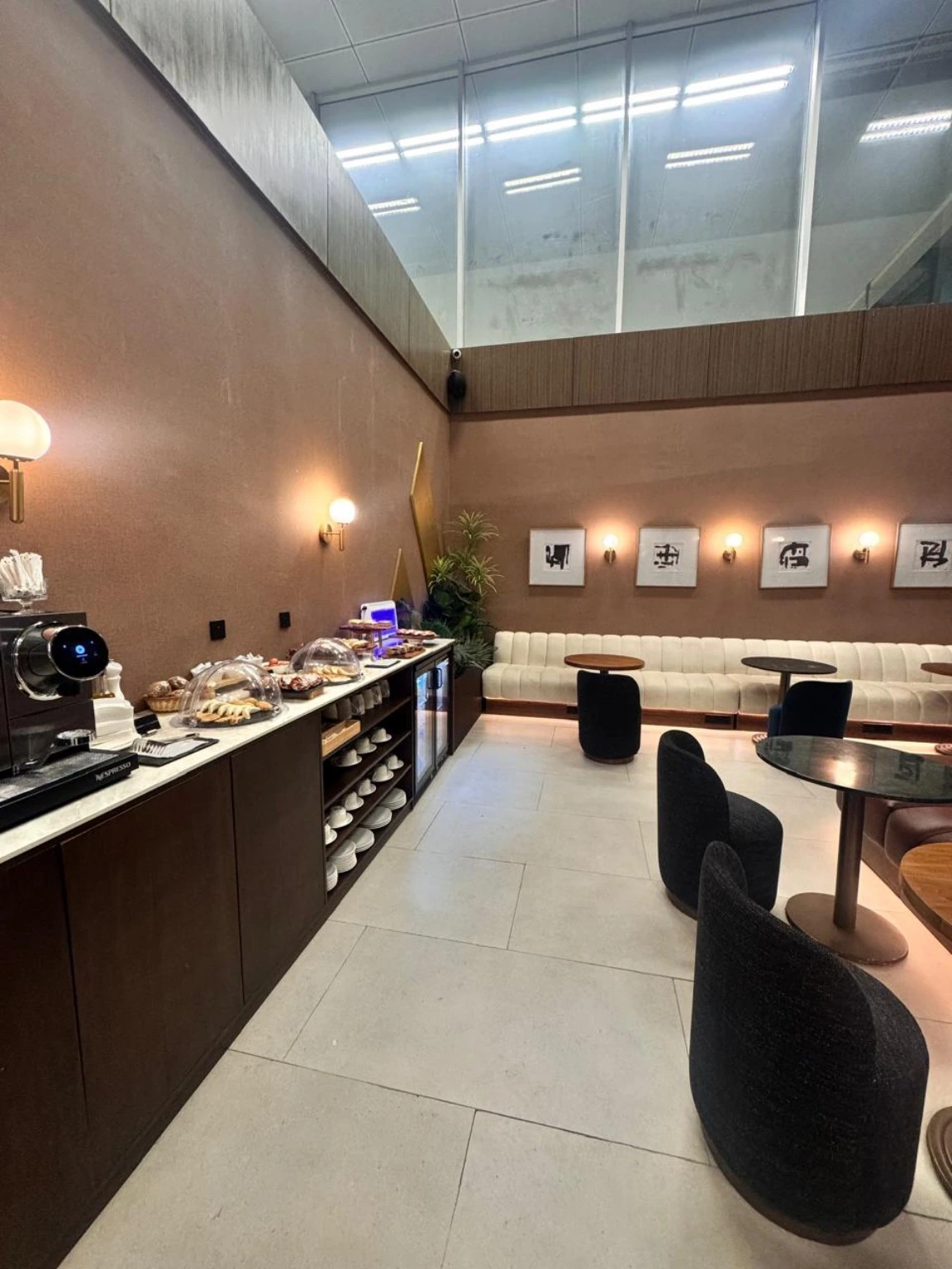 Lounge interior with a refreshment counter, coffee equipment, tables and seating.